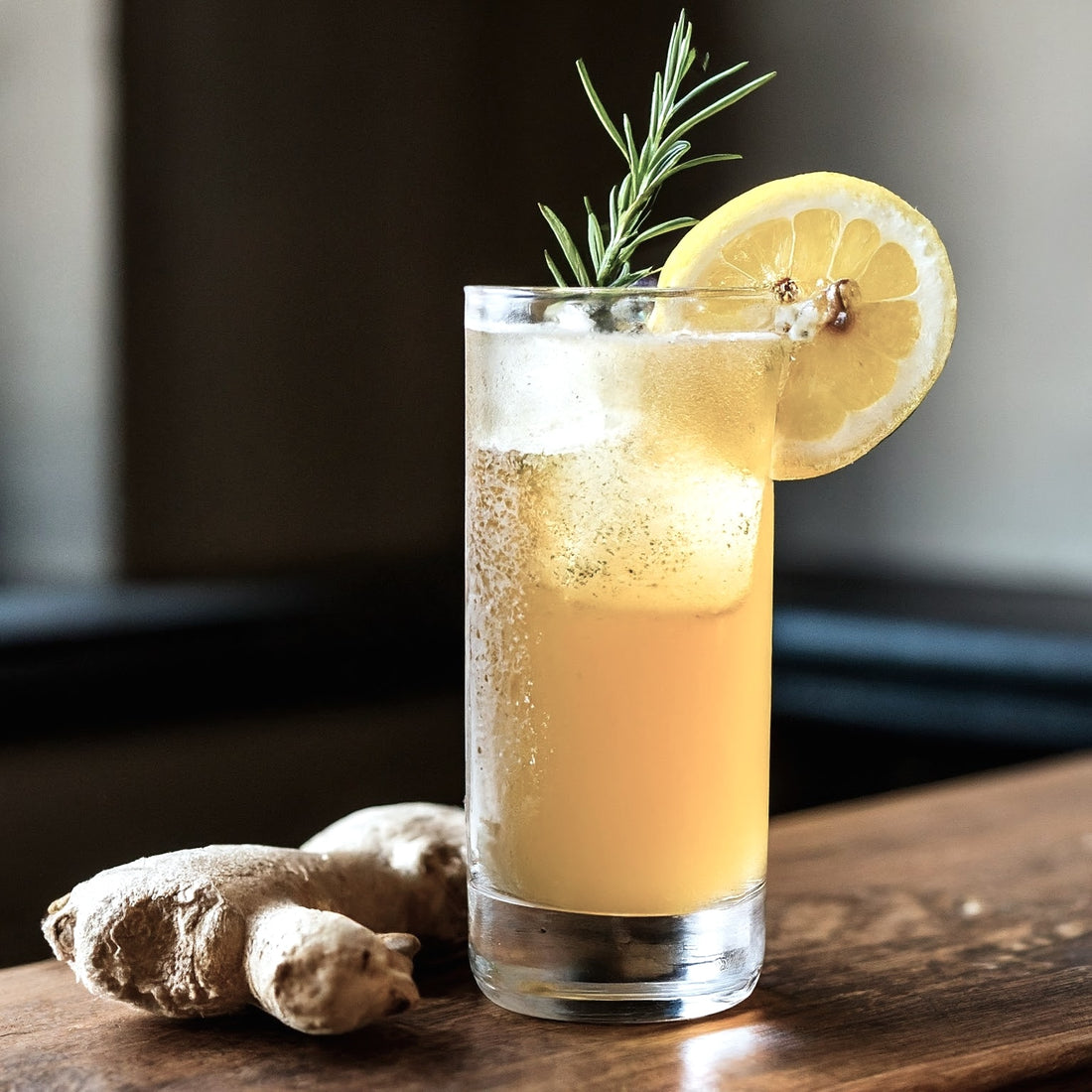 On a wooden surface stands a tall glass filled with an iced beverage made from Top Hat Provisions Extra Spicy Ginger Beer BIB Soda Syrup, garnished with lemon and rosemary. Nearby lie two ginger root pieces, enhancing the fresh look.