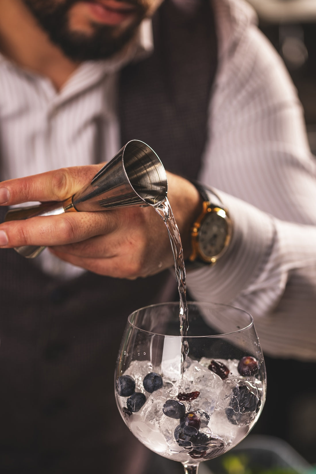 Bartender measuring gin into a Spanish gin and tonic goblet with berries and ice, small file, no crop