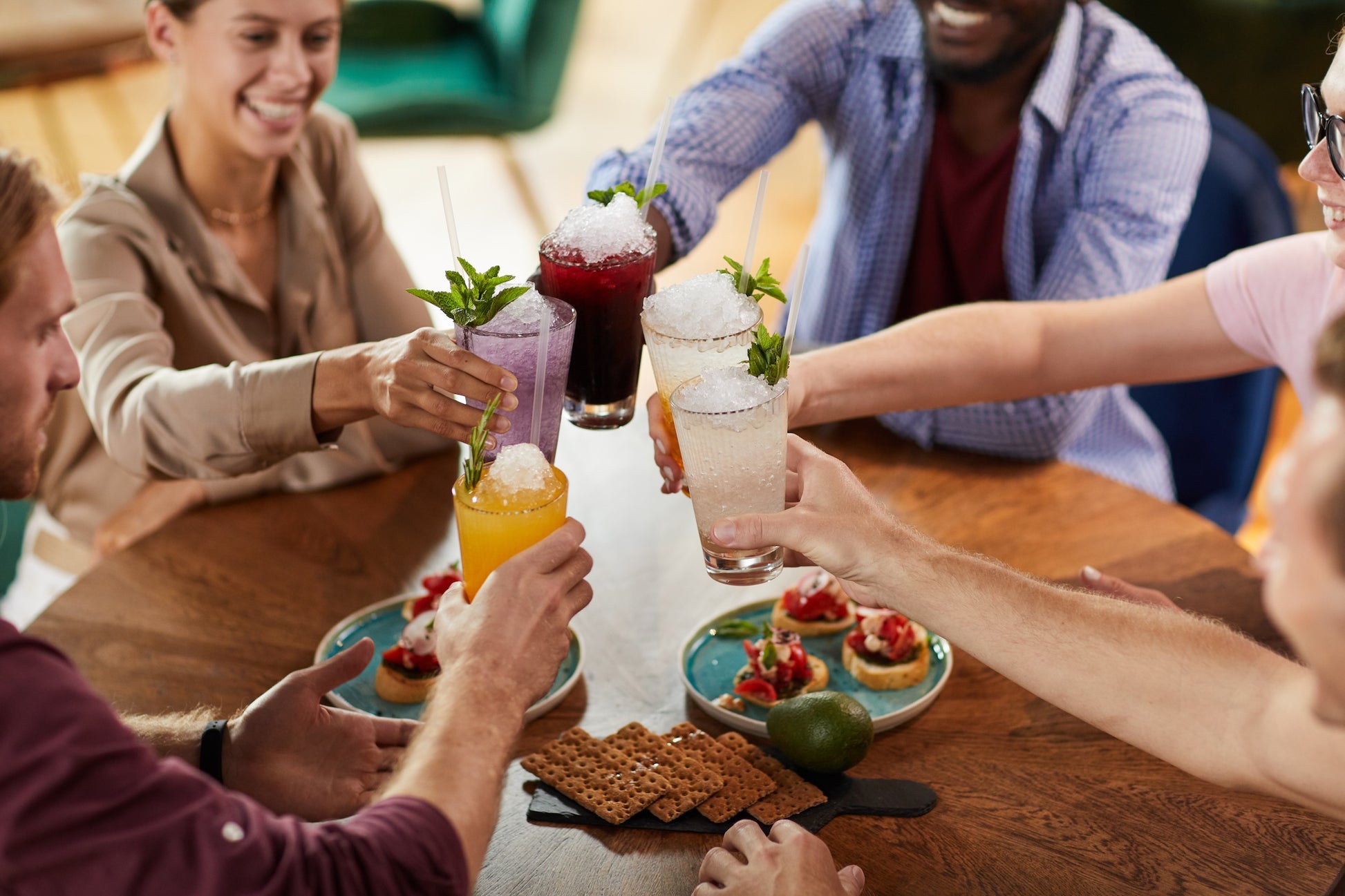 Group cheersing with butterfly and crushed ice cocktails at table with crackers