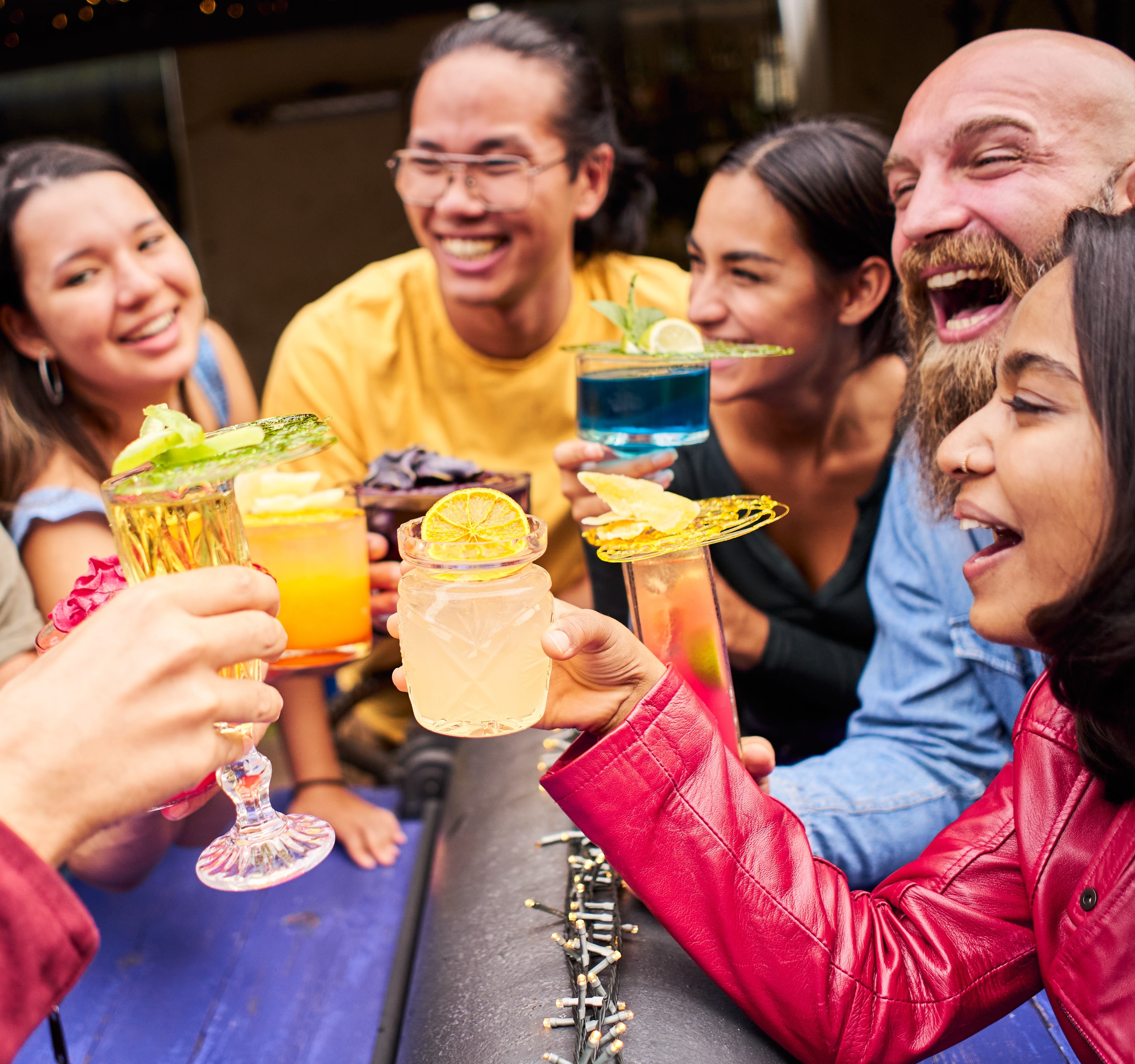 Group of cool people in their 30s drinking cocktails with drinks in the center, square crop