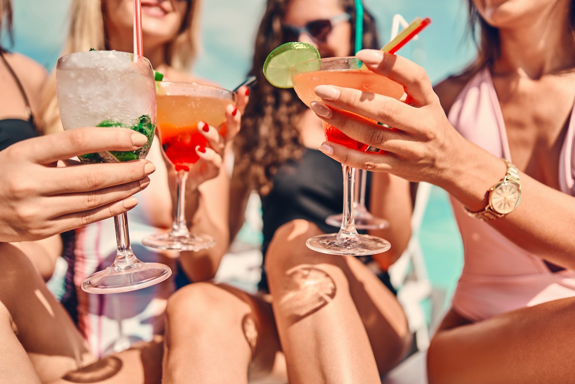 Four friends in swimwear toast with monk fruit sweetened, lime and mint-garnished cocktails by the pool. Theyre enjoying a summery vibe, using Top Hat Provisions Top Hat Keto Sugar Free Mixology Cocktail & Soda Syrup Combo Kits 32oz bottles.